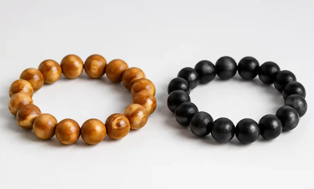 Side-by-side comparison of sandalwood and ebony wooden bead bracelets on neutral surface